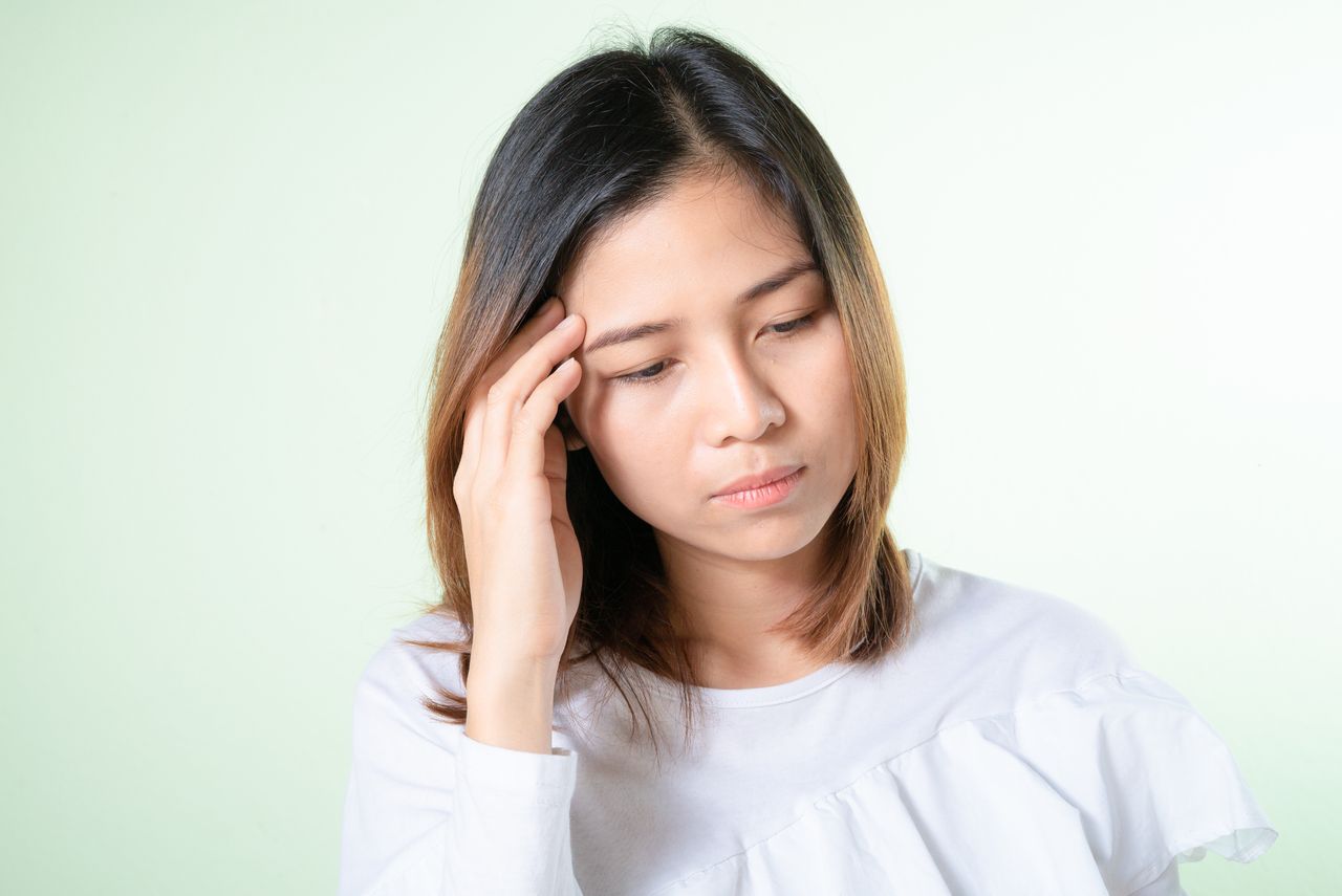 Contemplative young woman in a white top, deep in thought against a light background.