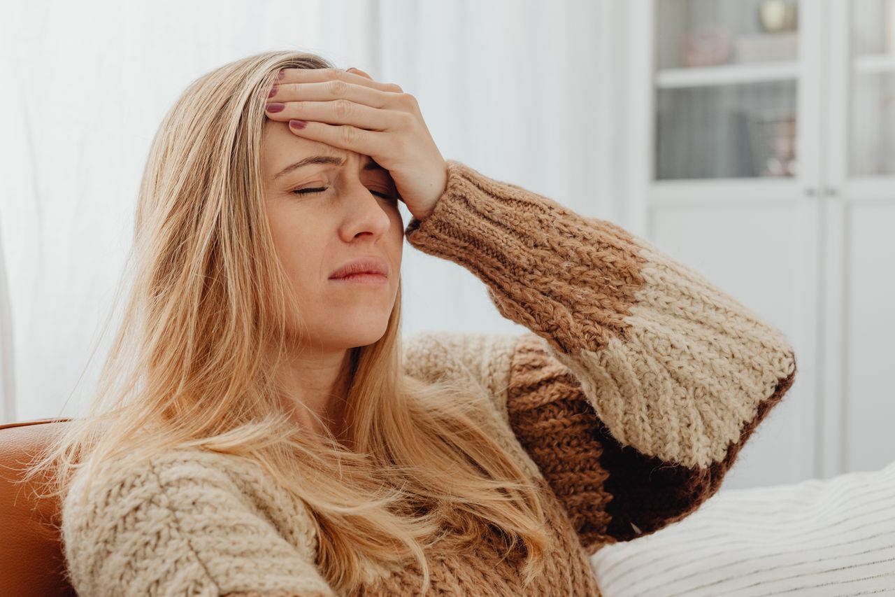 Close-up of a woman with a headache, hand on forehead, in a comfortable setting.